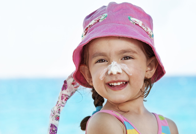 Smiling girl at the beach wearing pink hat and suncreen on her nose