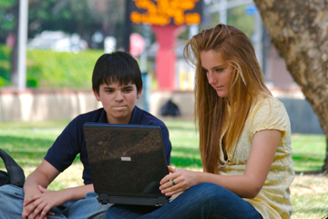 Boy and girl under a tree looking at a computer screen