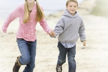 Sister and brother running and holding hands at the beach