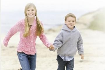 Smiling sister and brother holding hands at the beach