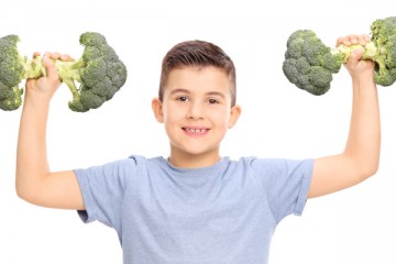 Boy holding up broccoli like bar bells