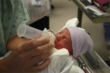 Infant with cap being fed a bottle