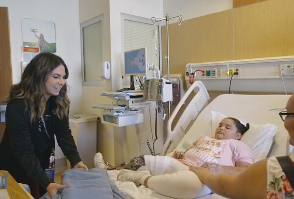 Child life specialist smiles at patient in bed during stay at CHOC's hematology/oncology unit