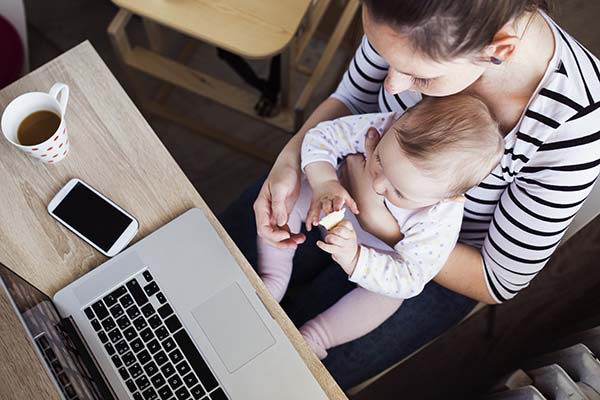 Mom holding baby at a desk in front of a laptop.