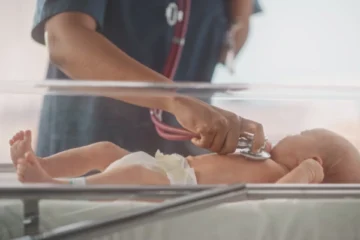 healthcare professional uses a stethoscope to monitor a newborn in an incubator, representing neonatal care and attention to infant health.