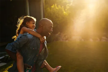 Dad giving daughter a piggy back ride, sunset