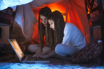 Portrait of two teenage sisters using laptop at night before going to bed