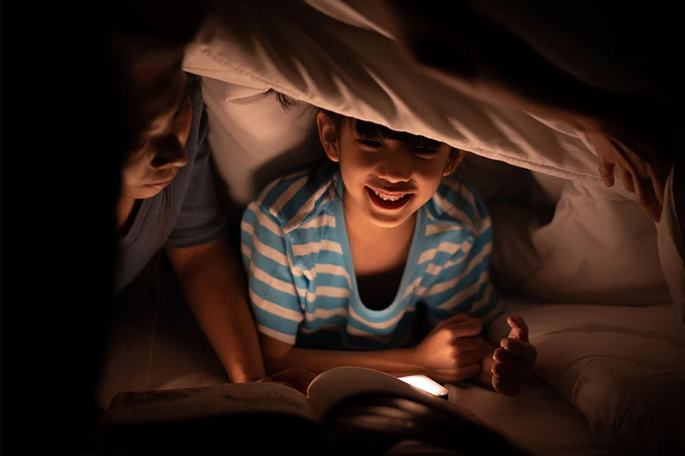 young child reading under the covers