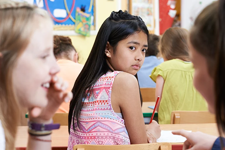 Niña infeliz siendo chismeada por sus compañeras de clase en el aula