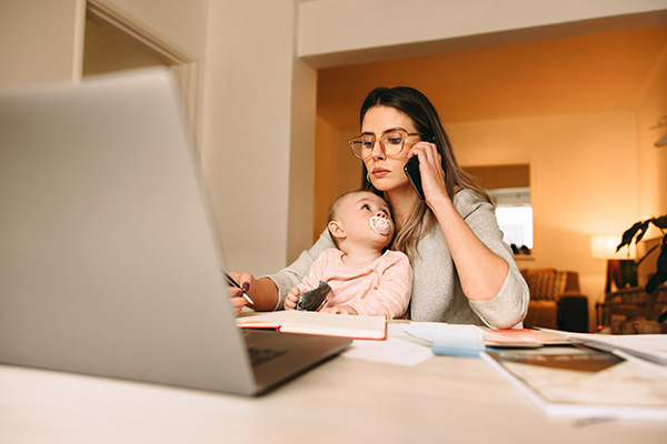Parent on the phone looking at compute with baby on their lap