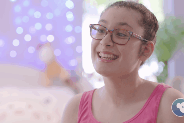 Teenage girl with glasses smiling in a bright room.