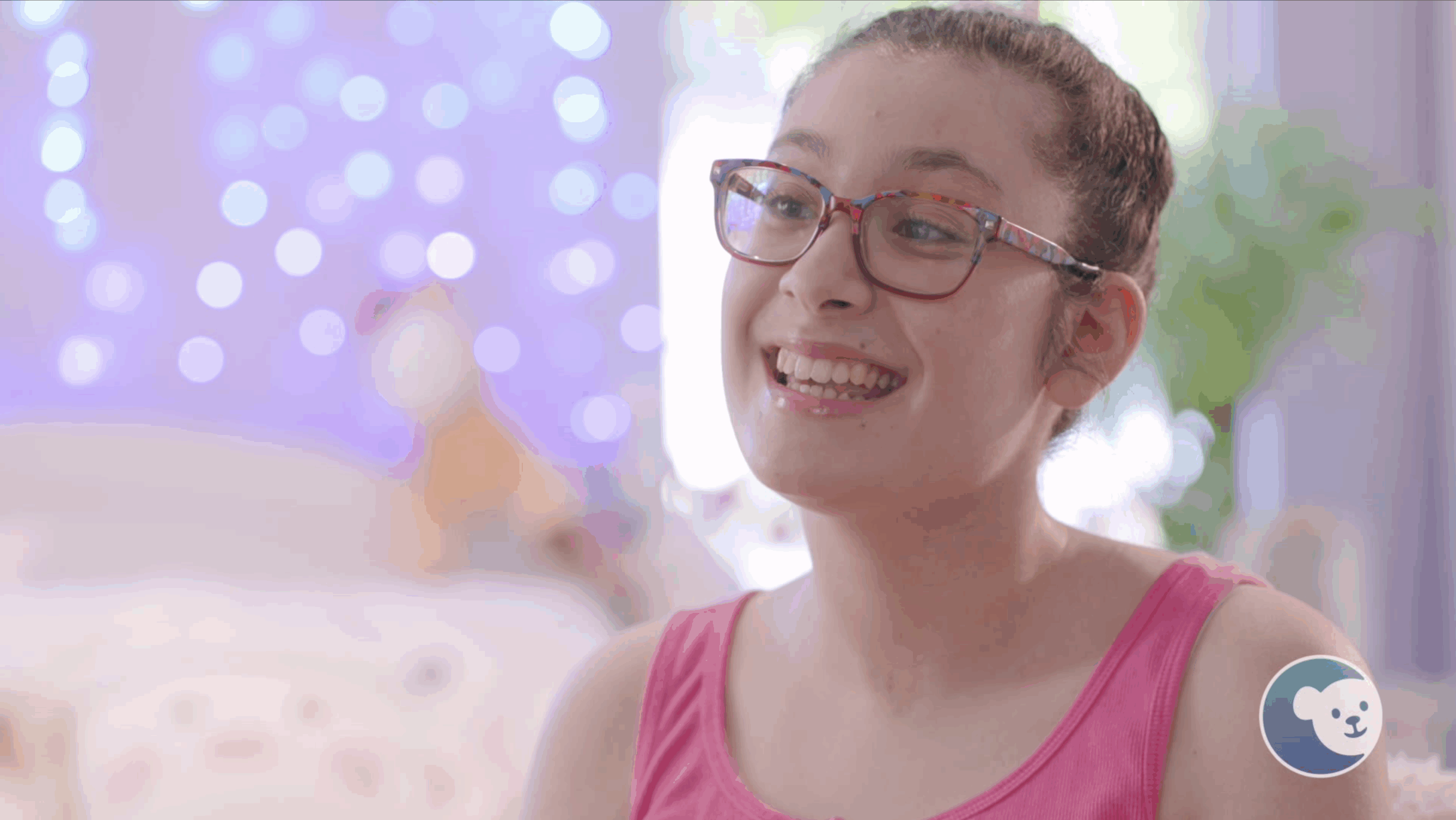Teenage girl with glasses smiling in a bright room.