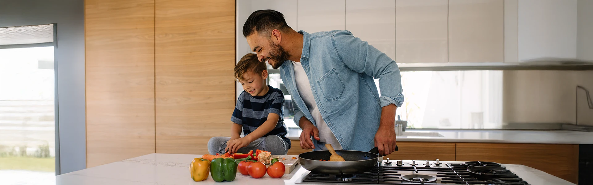 Smiling father watching little son cutting vegetables