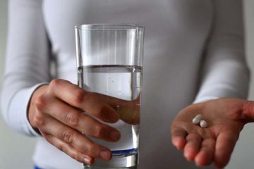 Woman holding glass of water and white pills