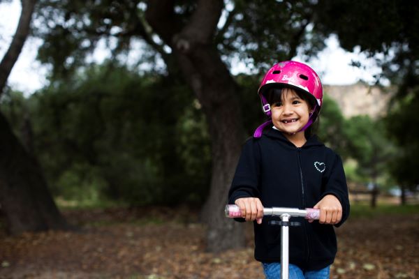 young girl wearing helmet and riding scooter